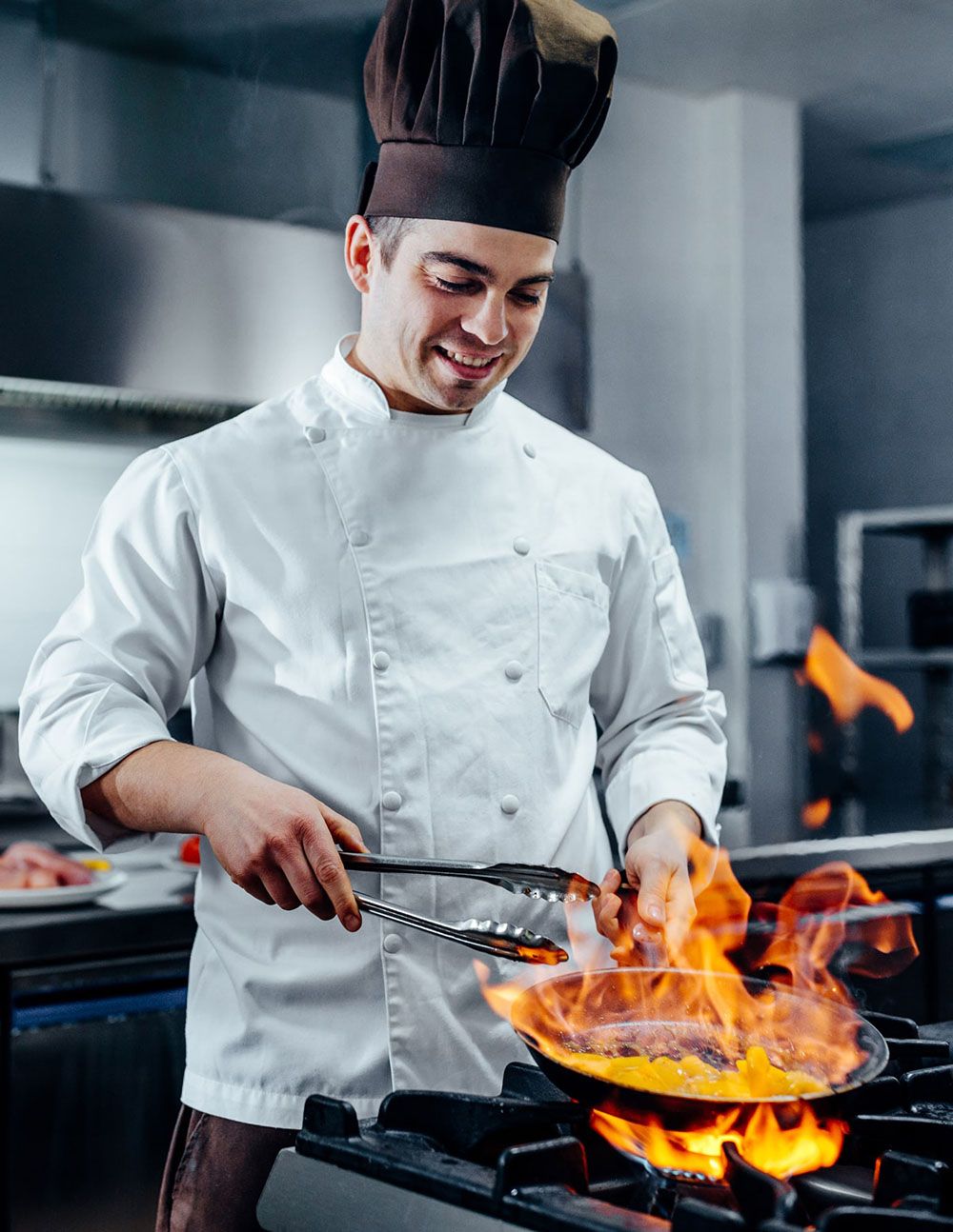 Chef cuisinier qui flambe une préparation dans une poèle