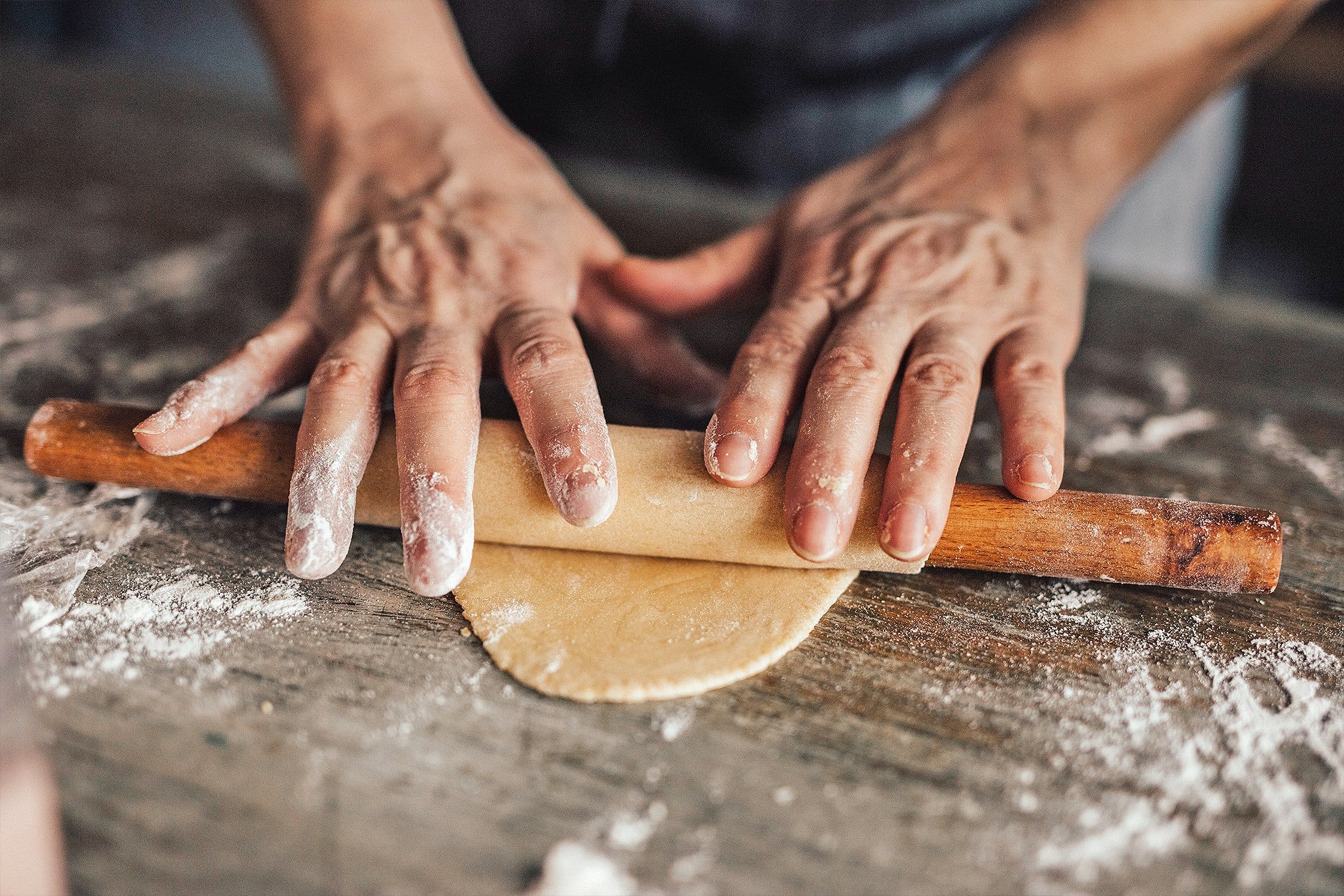 Plan rapproché sur les mains d'un pâtissier enroulant de la pâte autour d'un rouleau à pâtisserie