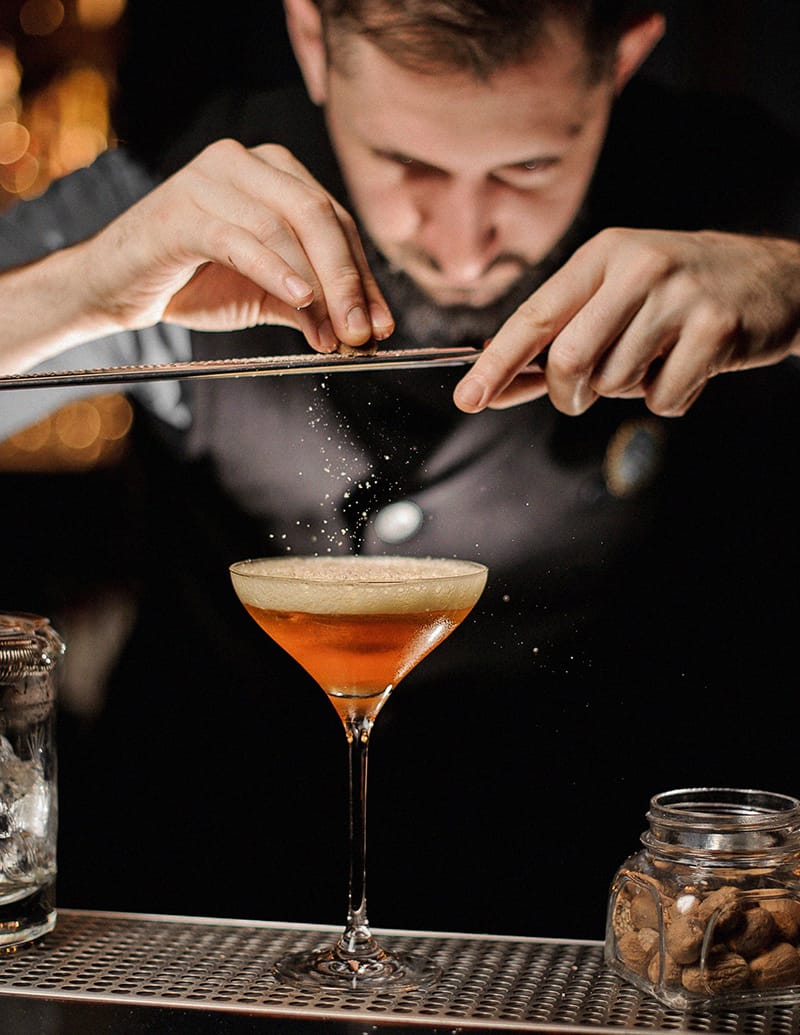 Plan rapproché d'un barman râpant un aliment sur un cocktail