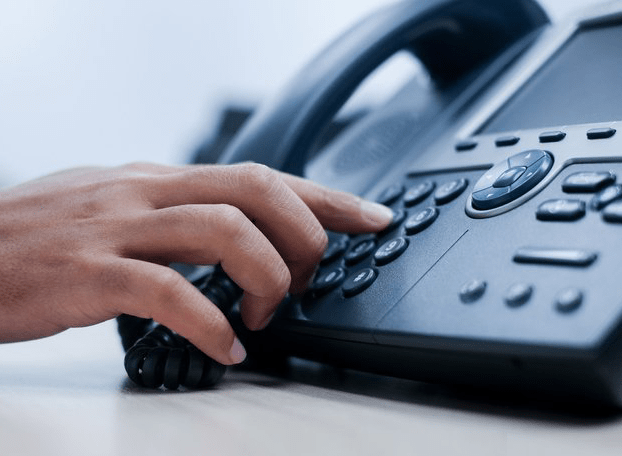 Hands pressing a number on a landline phone representing how you can punch work hours with a landline telephone