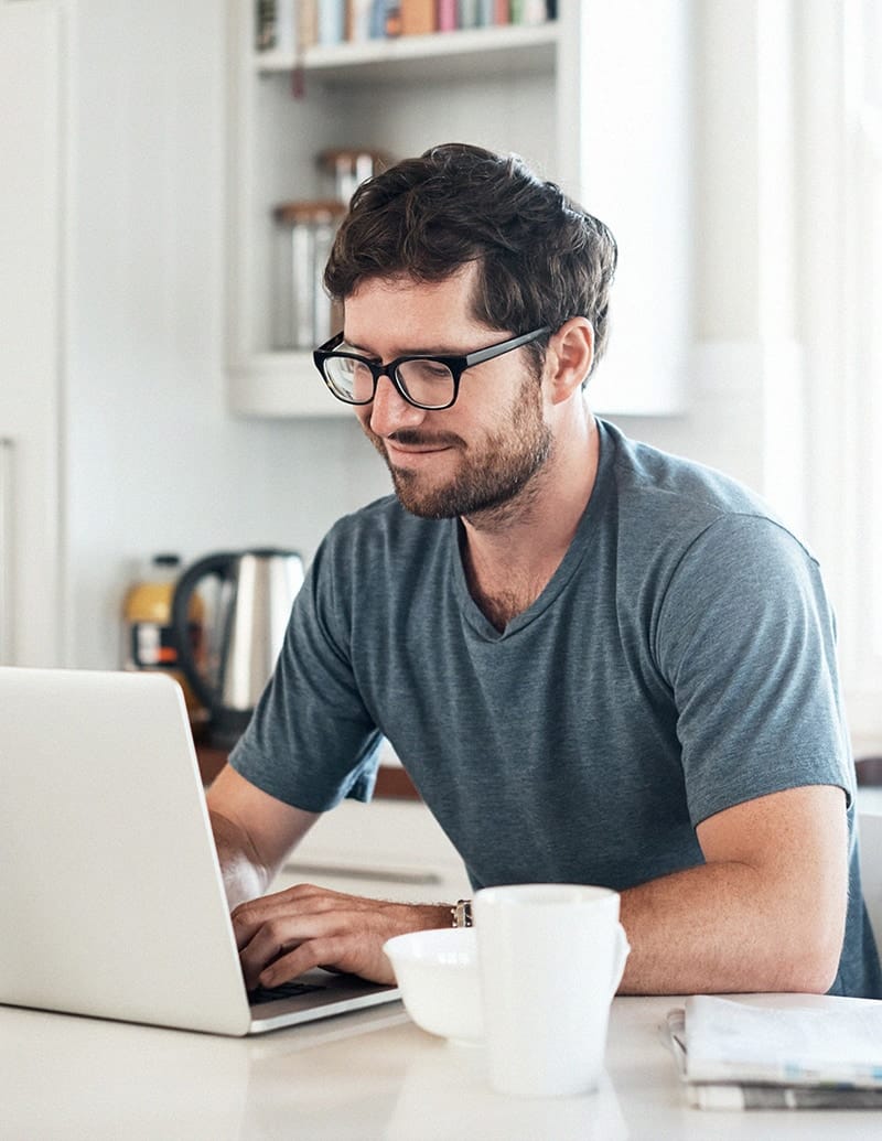 Homme qui recherche un logiciel de gestion d'horaires sur son ordinateur en déjeunant à la maison