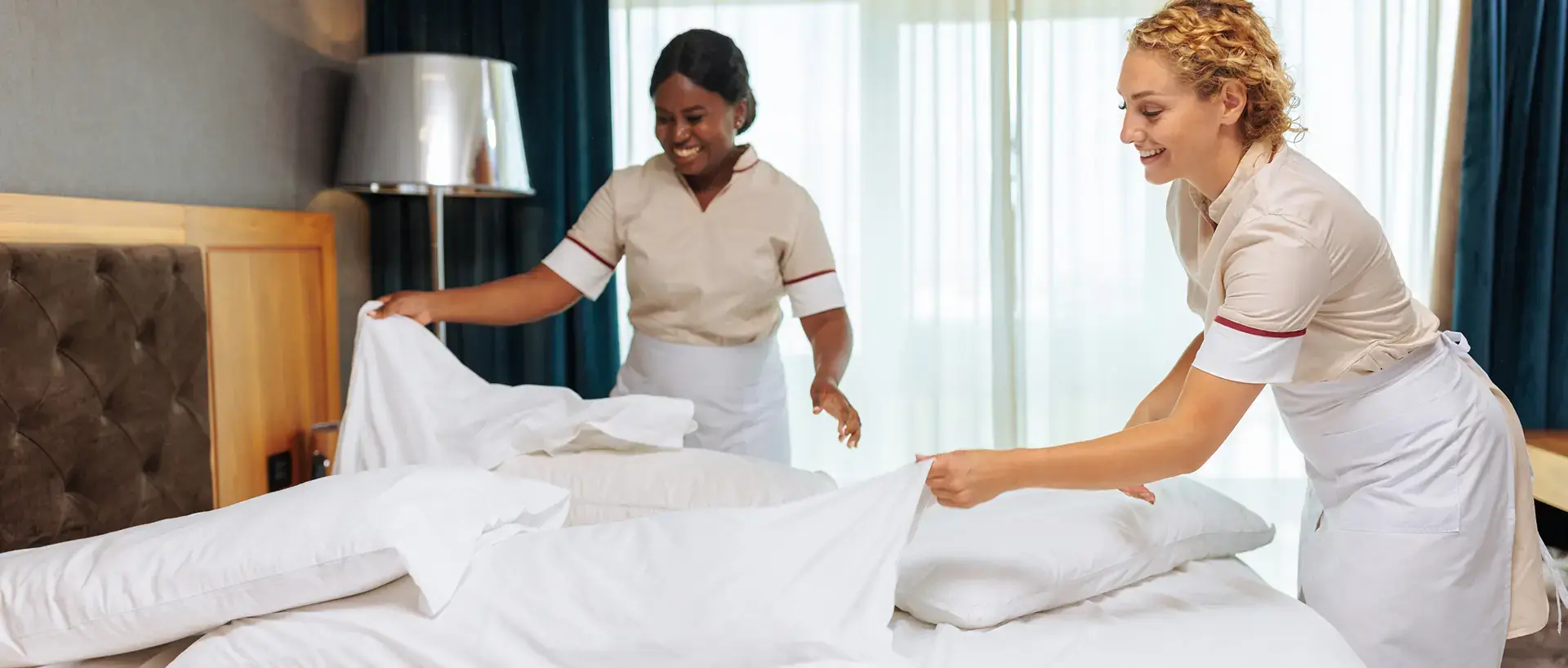 Two housekeepers preparing a hotel bed.