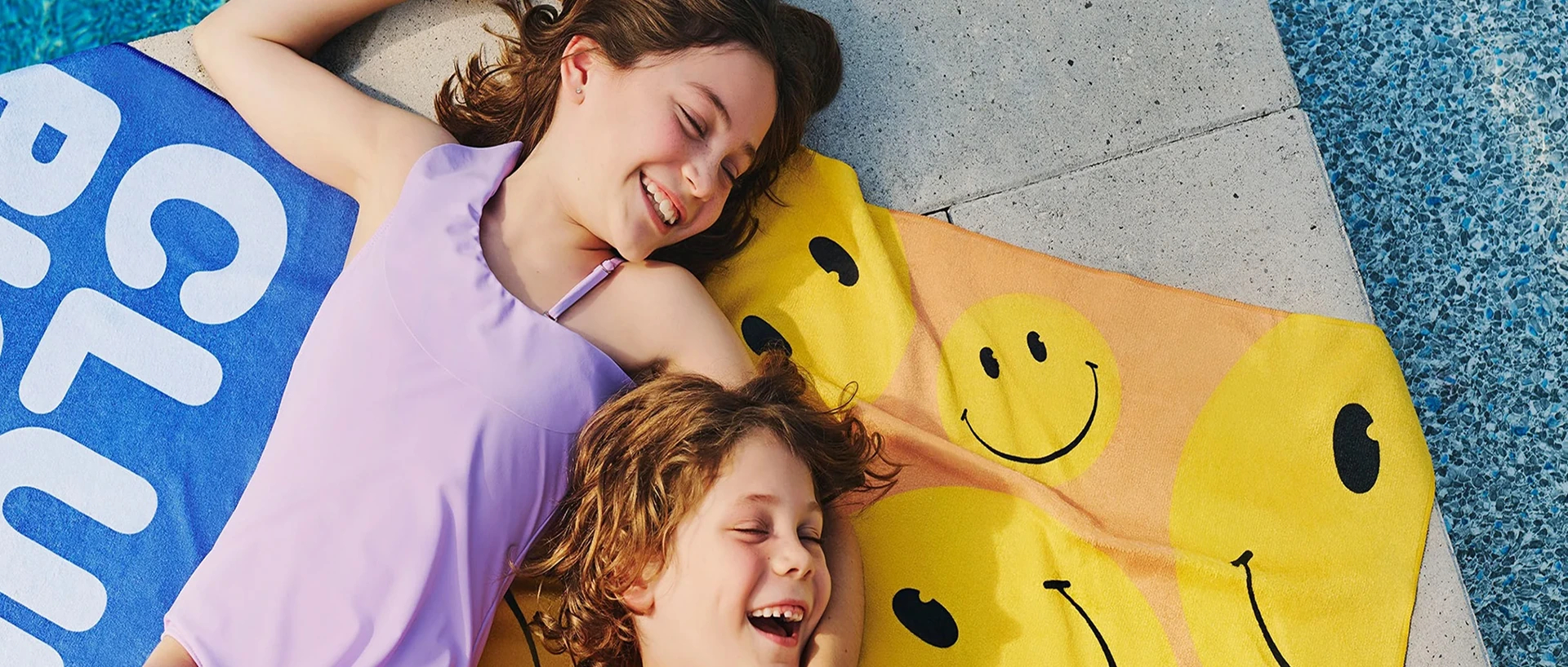 Deux enfants couchés sur une serviette de plage au bord de la piscine.