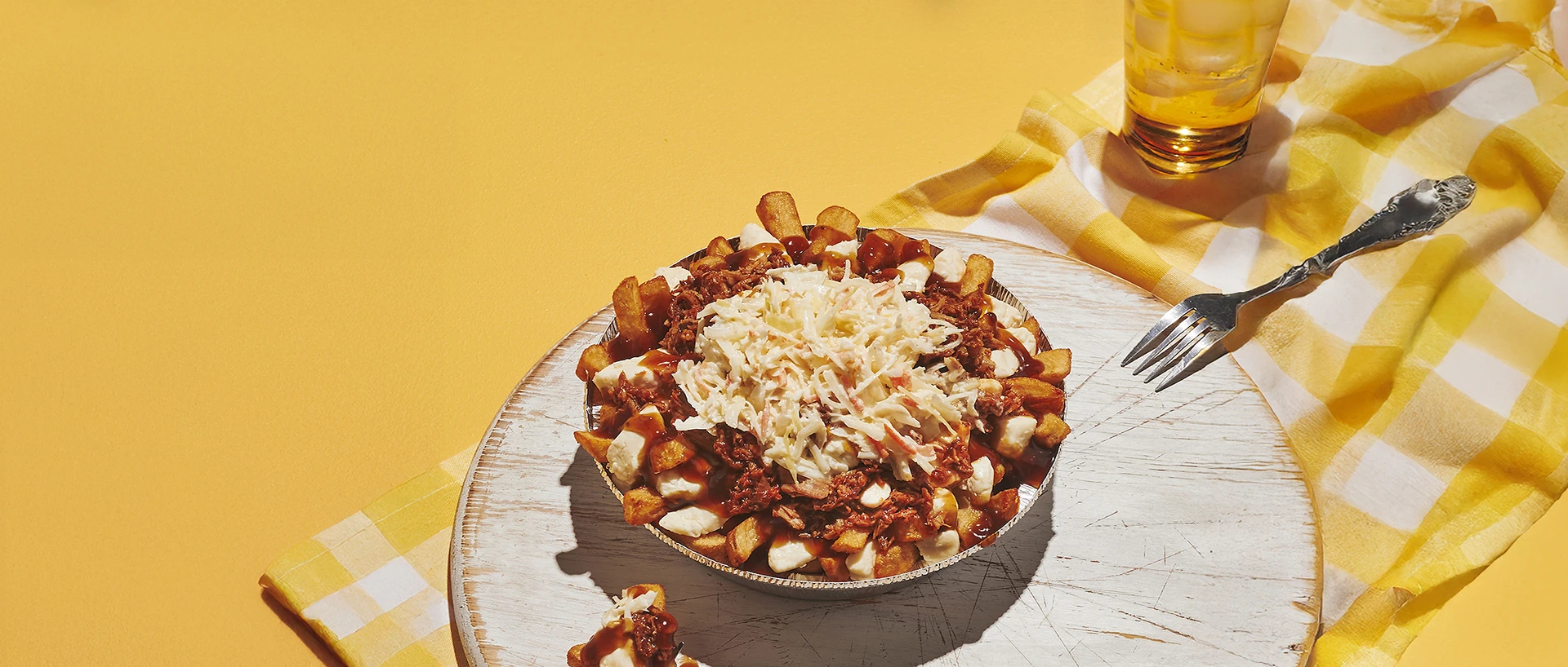 Vue en plongée sur une poutine posée sur un plateau. Le fond est de couleur jaune.