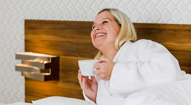 Cliente du Littoral Hôtel & Spa en peignoir couchée et satisfaite de sa tasse blanche