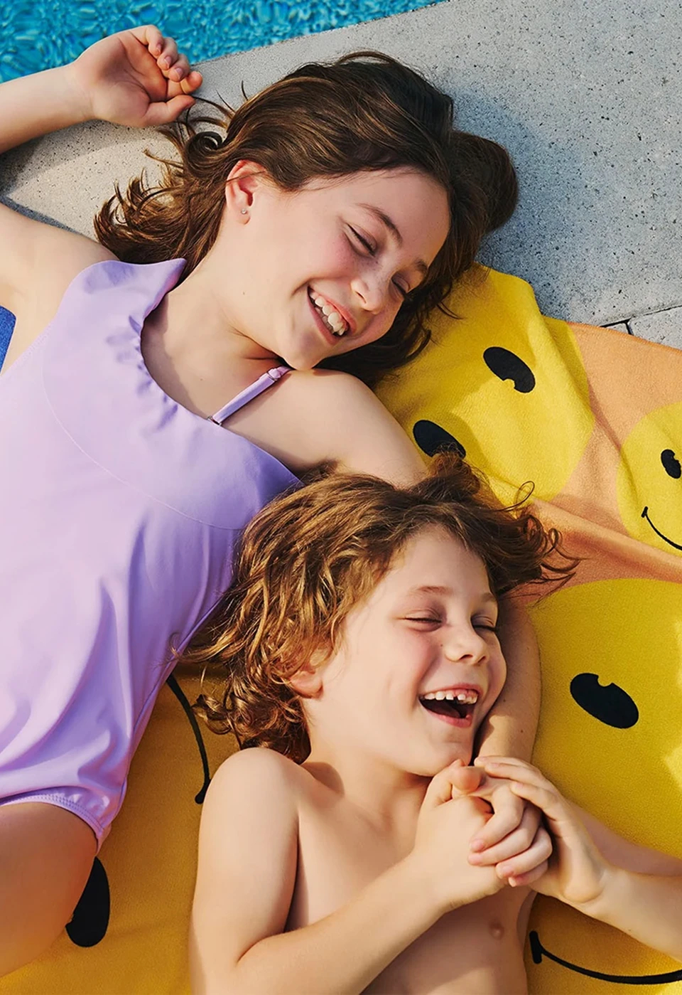 Deux enfants couchés sur une serviette de plage au bord de la piscine.