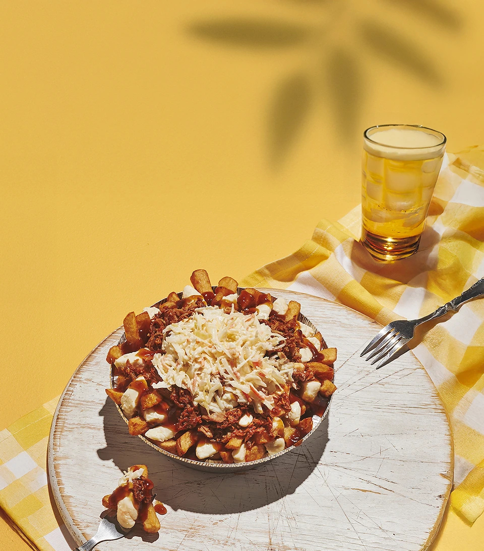 Vue en plongée sur une poutine posée sur un plateau. Le fond est de couleur jaune.